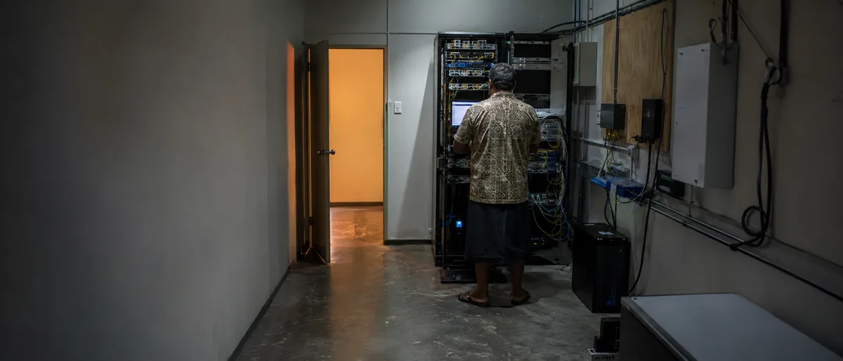 A lone IT worker at a server rack in an otherwise empty comms room
